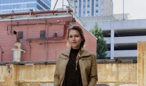 Picture of Cassie Ball in a tan leather jacket with Winston-Salem buildings in the background