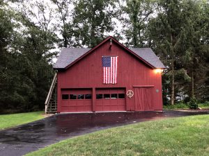 Picture of a Red Barn in forest with American Flag hanging and peace-sign wreath
