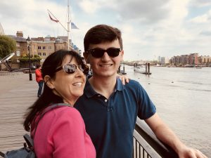 Laurence Roberts in a blue shirt with his mother, who is in pink. They are leaning against a railing near a body of water.